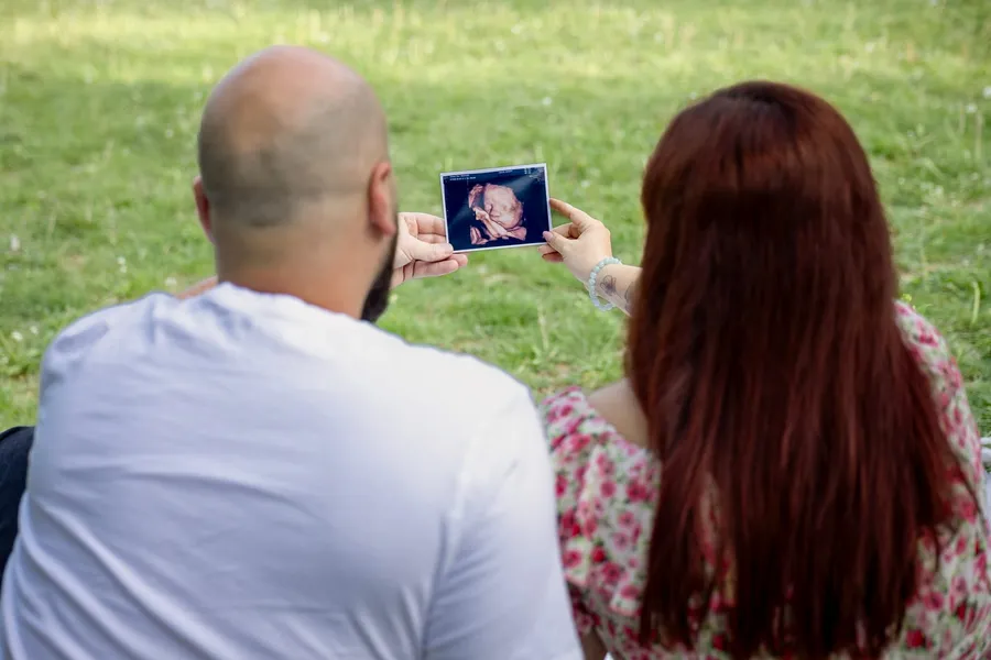 Pár napfényes gyepen ülve nézi babájuk ultrahangképét — Gáspár Enikő Photography