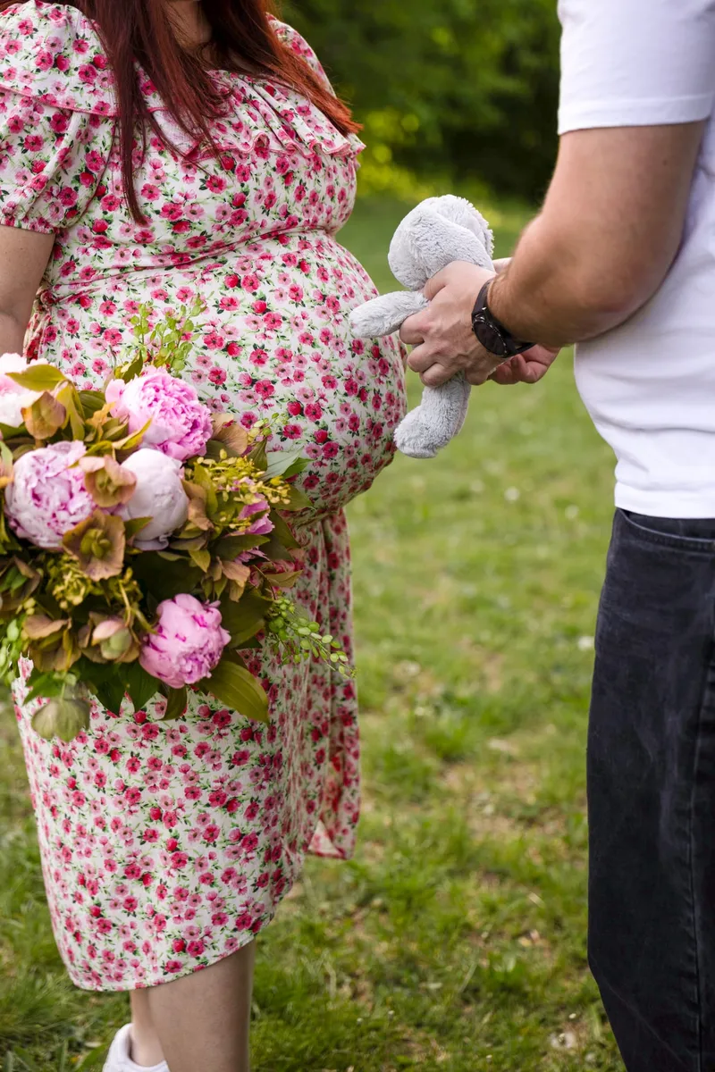Várandós nő pünkösdi rózsa csokrot tart, párja plüss játékkal áll mellette a parkban — Gáspár Enikő Photography