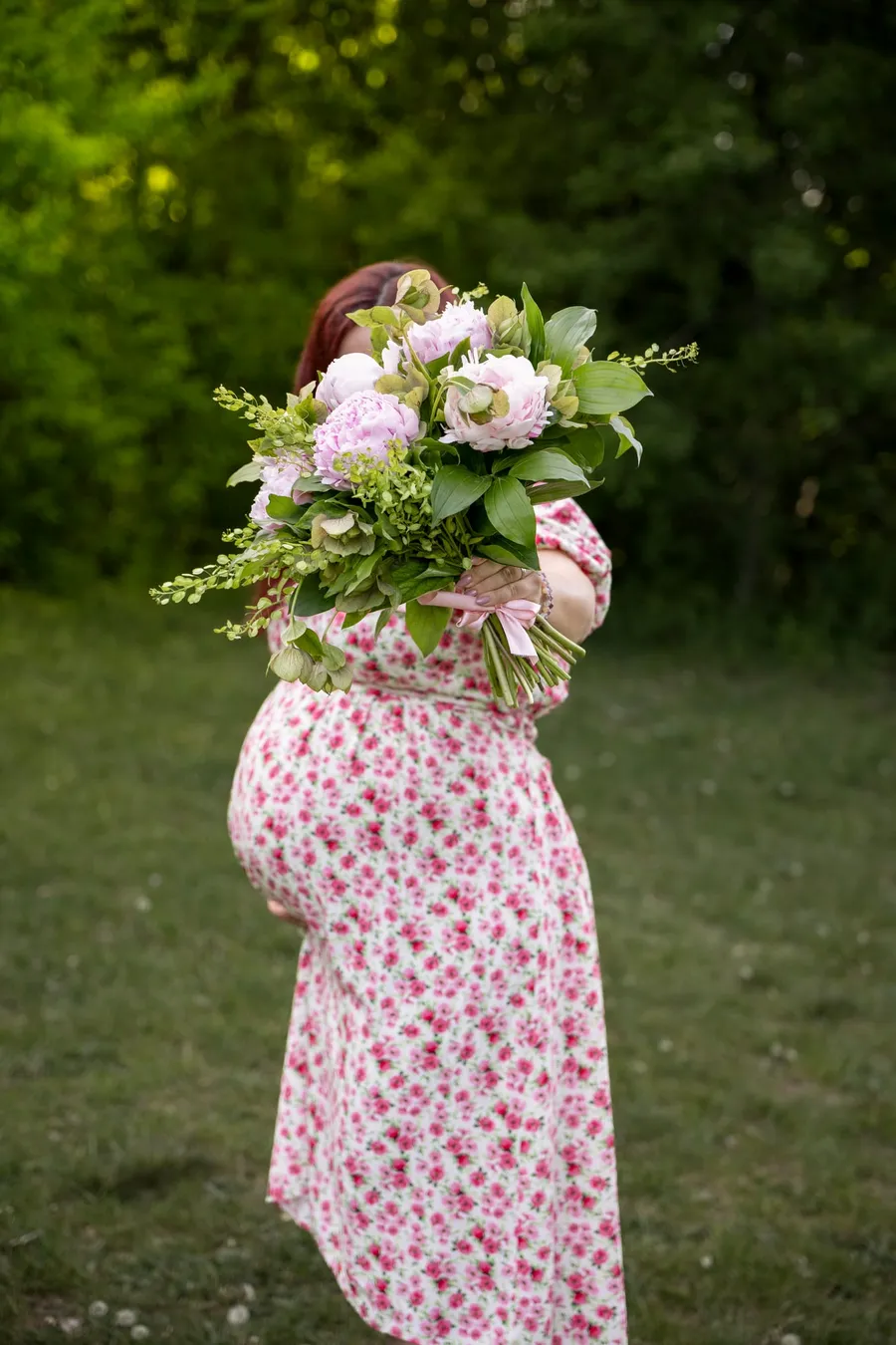 Várandós anya hátulról fotózva, nagy rózsaszín pünkösdi rózsa csokrot tart zöld parkban — Gáspár Enikő Photography